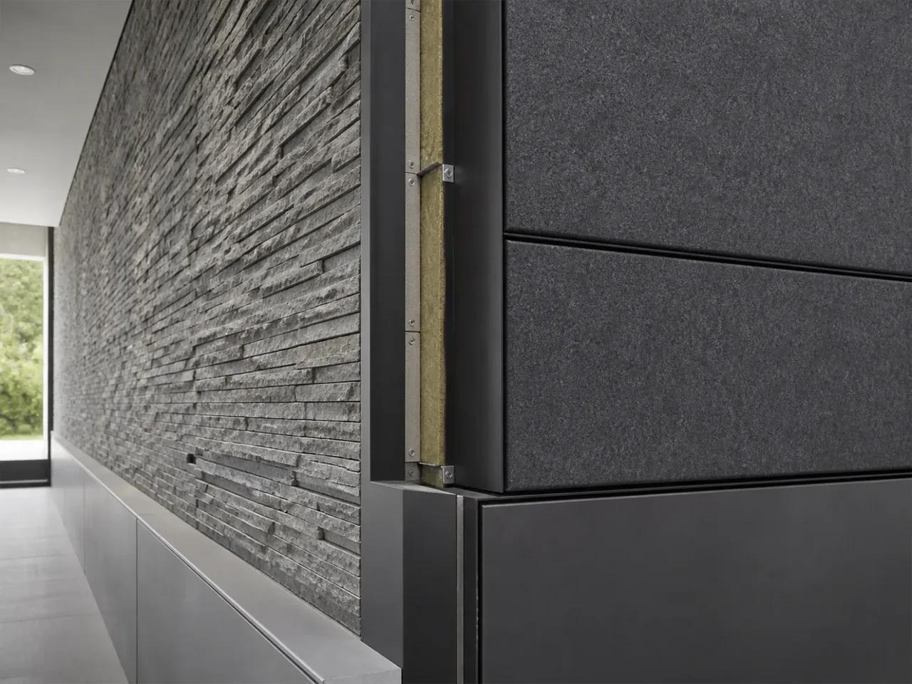Interior-to-exterior wall transition showing stacked stone veneer meeting dark cladding panels with exposed metal carrier channels and mineral wool cavity insulation