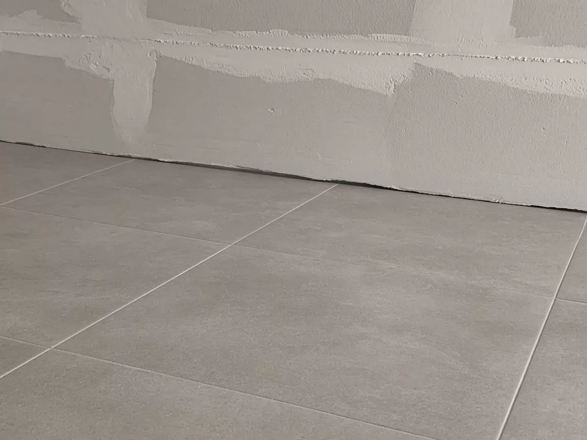 Ceramic floor tiles stopping at an unfinished wall, with a narrow dark line along the wall