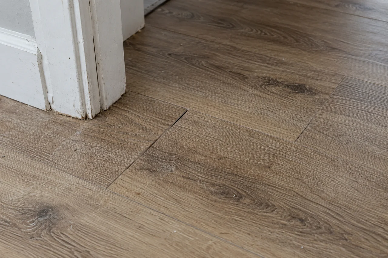 An open end joint in oak-look floor planks beside a scuffed white door jamb